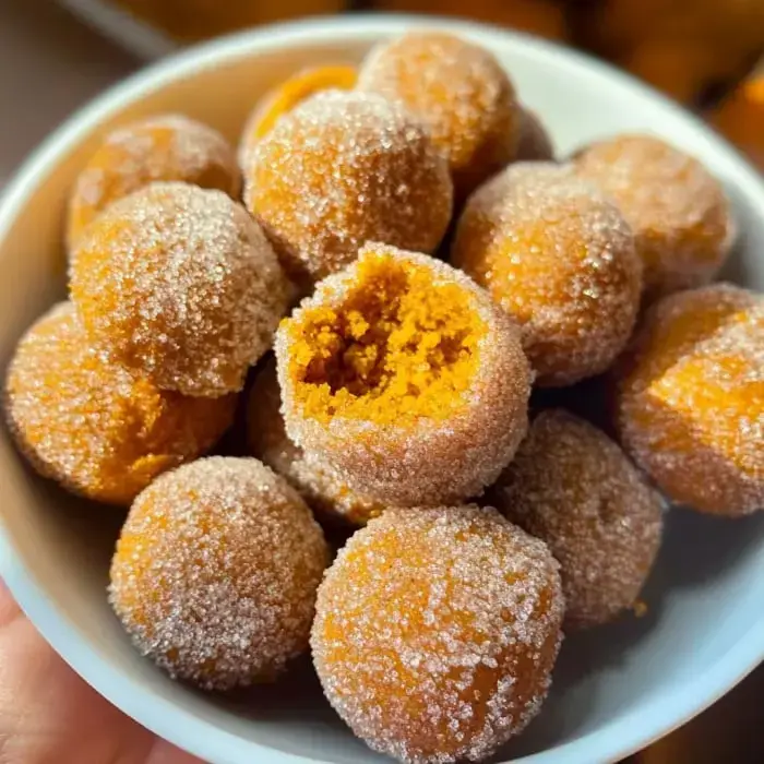 Round orange snacks rolled in sugar, one has a bite taken out, piled in a bowl.